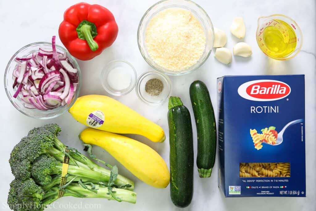 Ingredients for Pasta Primavera, including rotini pasta, zucchini, yellow squash, red pepper, red onion, broccoli, olive oil, garlic cloves, Parmesan cheese, salt and pepper.