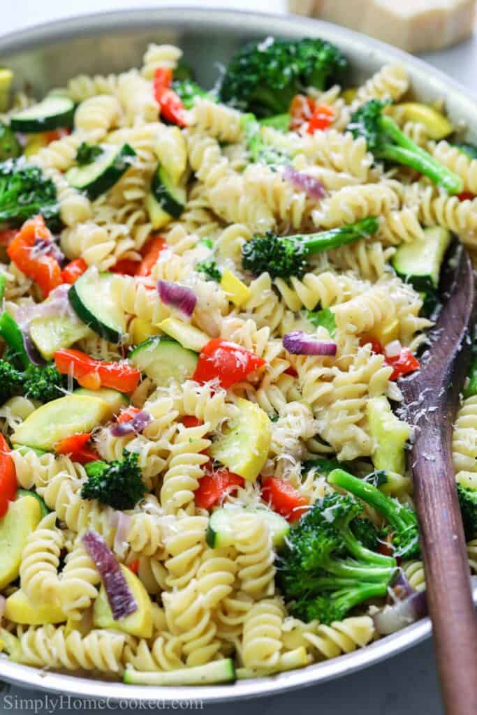 Vertical image of Pasta Primavera in a pan with a wooden spoon