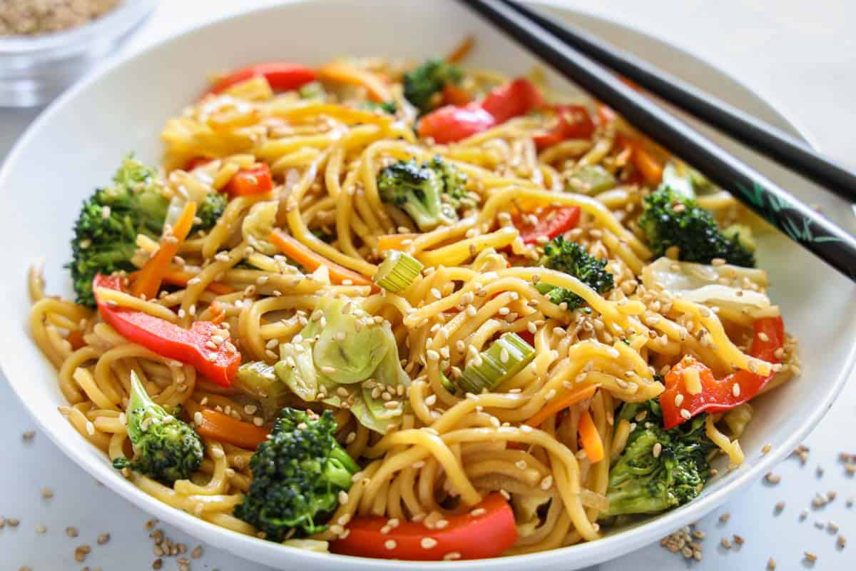 Horizontal image of a bowl of Chow Mein with sesame seeds sprinkled on top and chopsticks on the side