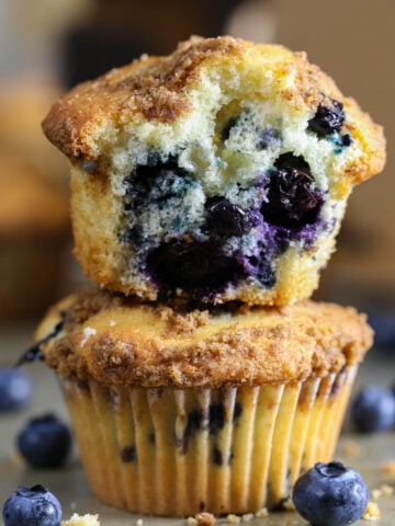 Vertical image of blueberry muffins stacked on each other, one missing a bite