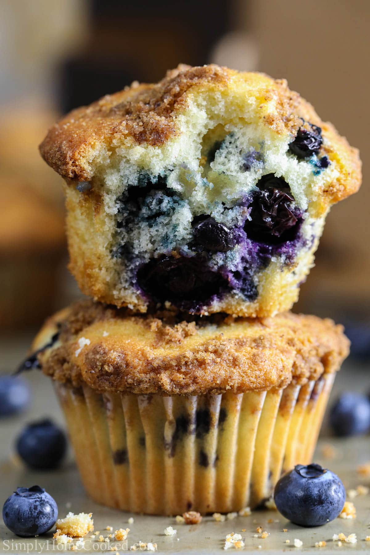 Vertical image of blueberry muffins stacked on each other, one missing a bite