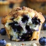 Horizontal image of a Blueberry Muffin with a bite missing and blueberries nearby