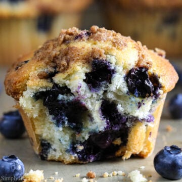 Horizontal image of a Blueberry Muffin with a bite missing and blueberries nearby
