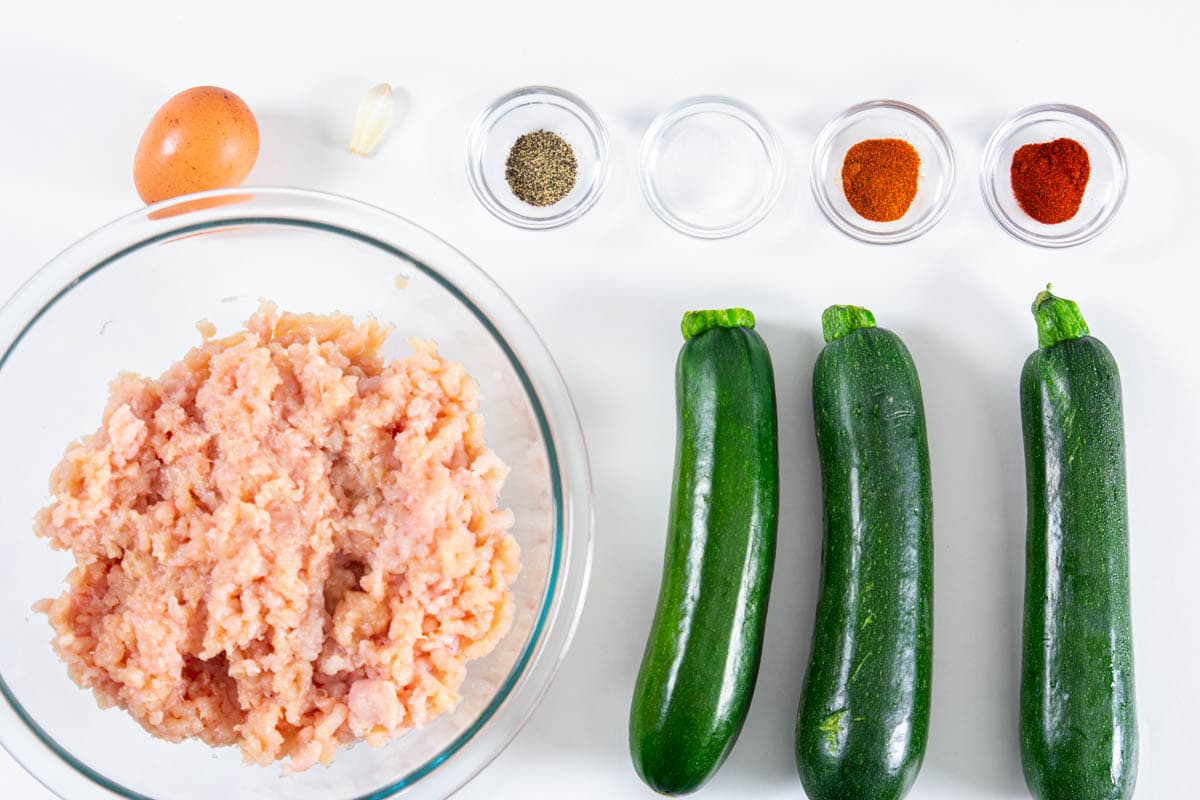 Ingredients for Chicken Fritters with Zucchini, including ground chicken, zucchini, garlic clove, egg, salt, pepper, cayenne, and paprika.