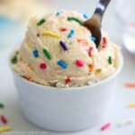close up image of edible sugar cookie dough in a white bowl with rainbow sprinkles on top