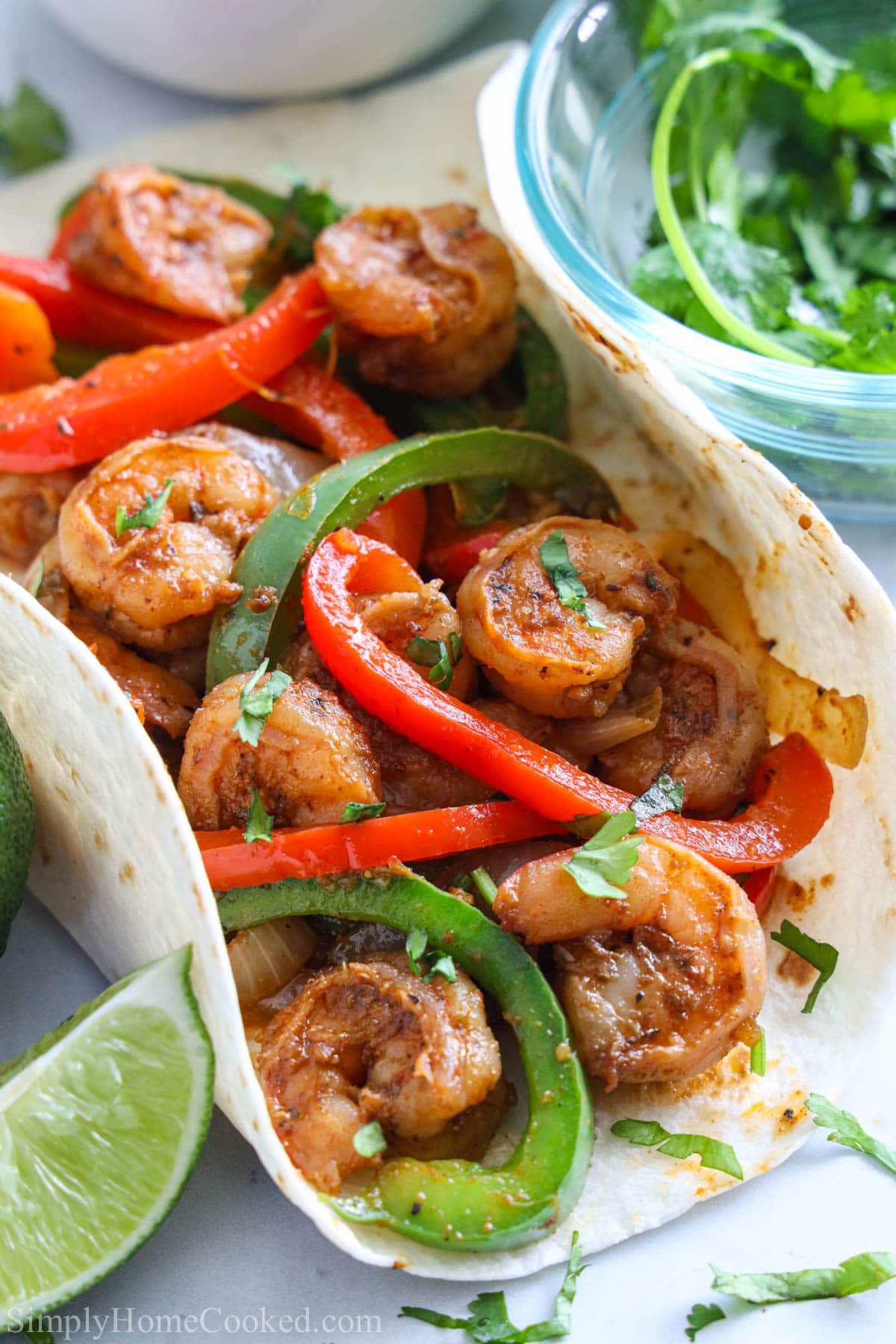 Vertical close up of Shrimp Fajitas in a flour tortilla, cilantro and a lime wedge on the side.
