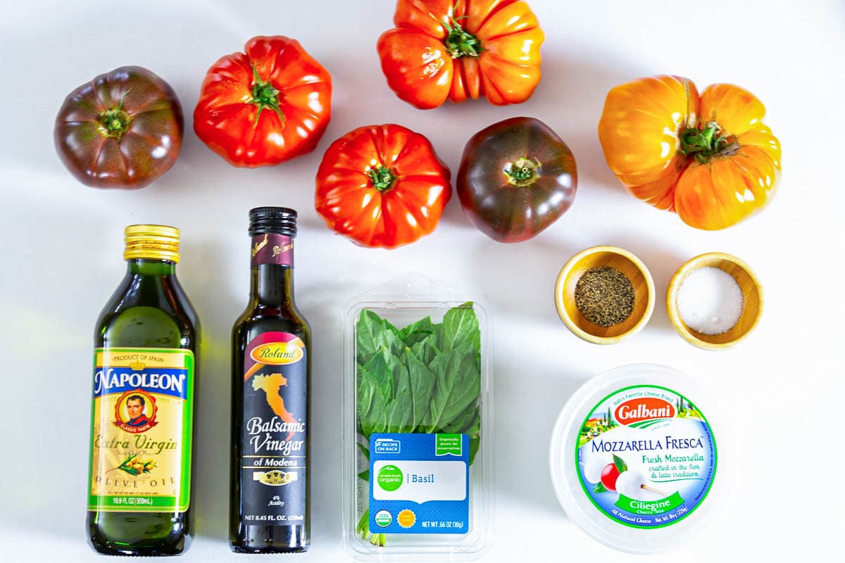 Ingredients for Caprese Salad, including heirloom tomatoes, mozzarella, basil, olive oil, balsamic vinegar, salt, and pepper.