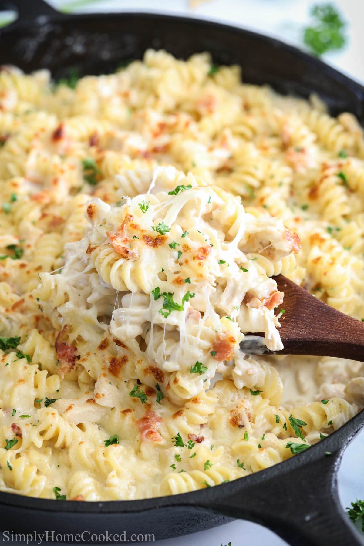 Vertical image of a close up of Chicken Bacon Ranch Pasta and a wooden spoon in a skillet
