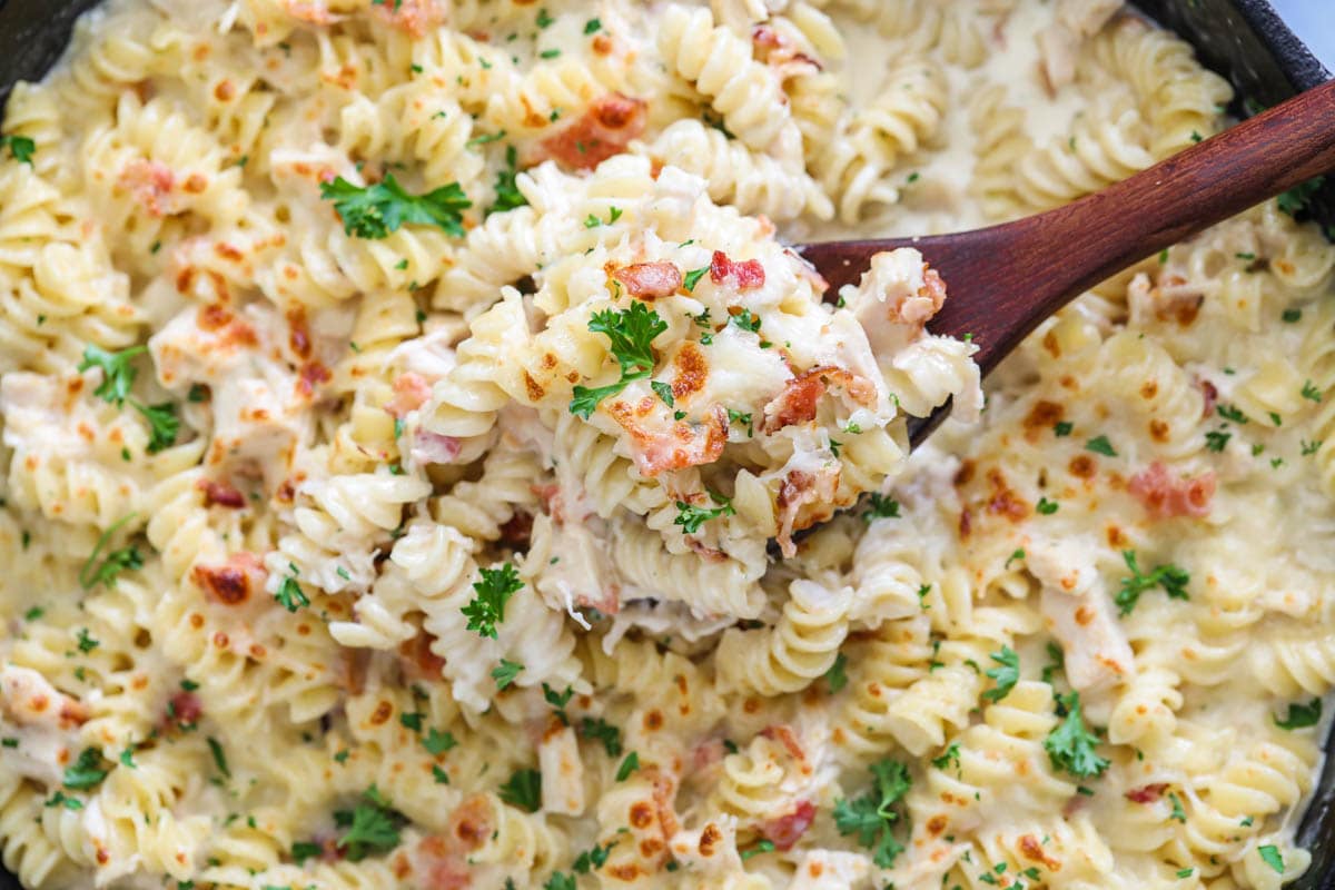 Horizontal image of a close up of Chicken Bacon Ranch Pasta and a wooden spoon in a skillet