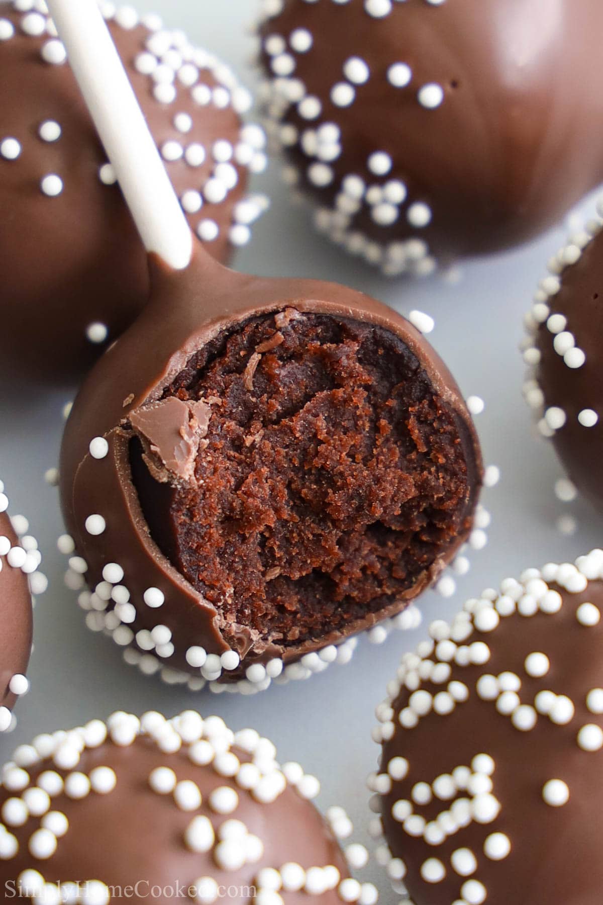 Closeup of a Chocolate Cake Pop with nonpareils, one with a bite missing.