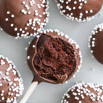 square image of Chocolate cake pops covered in nonpareils, one with a bite missing.