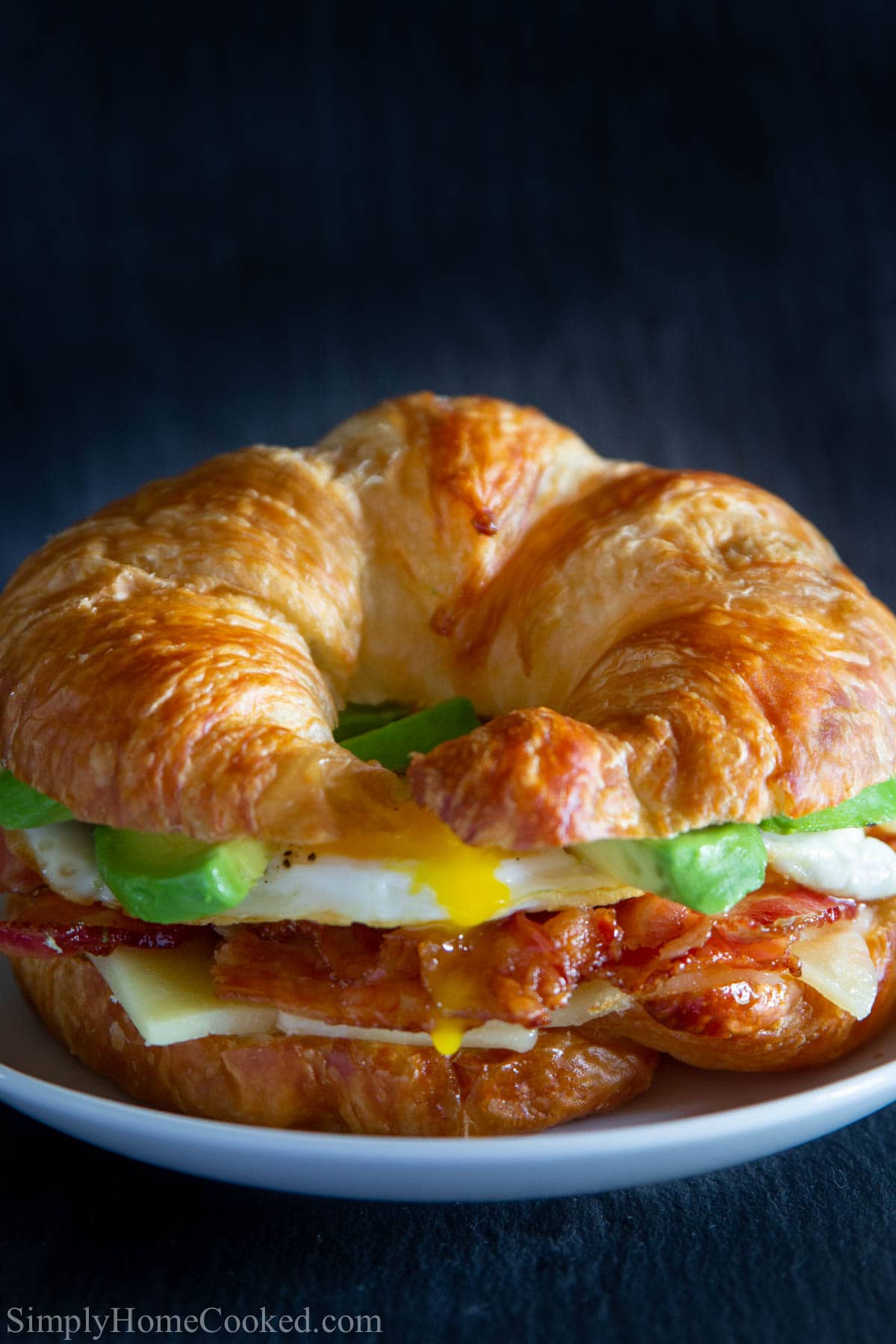 close up image of a croissant breakfast sandwich on a white plate