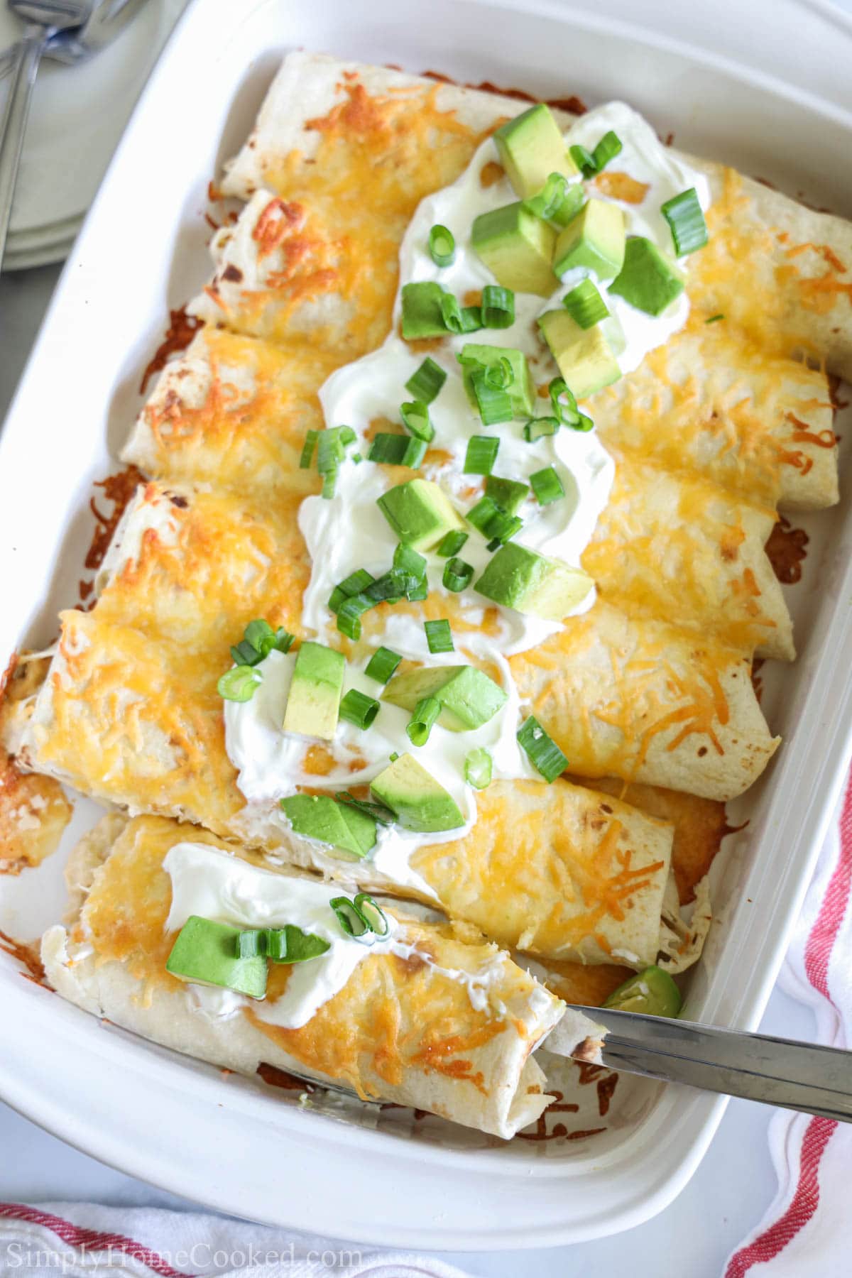 Overhead image of Easy Chicken Enchiladas with sour cream on top and a spoon lifting one out