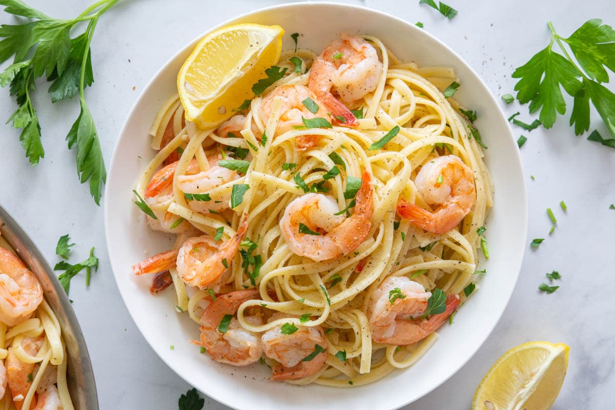 a close up of shrimp linguine in a white plate with lemons and parsley on top