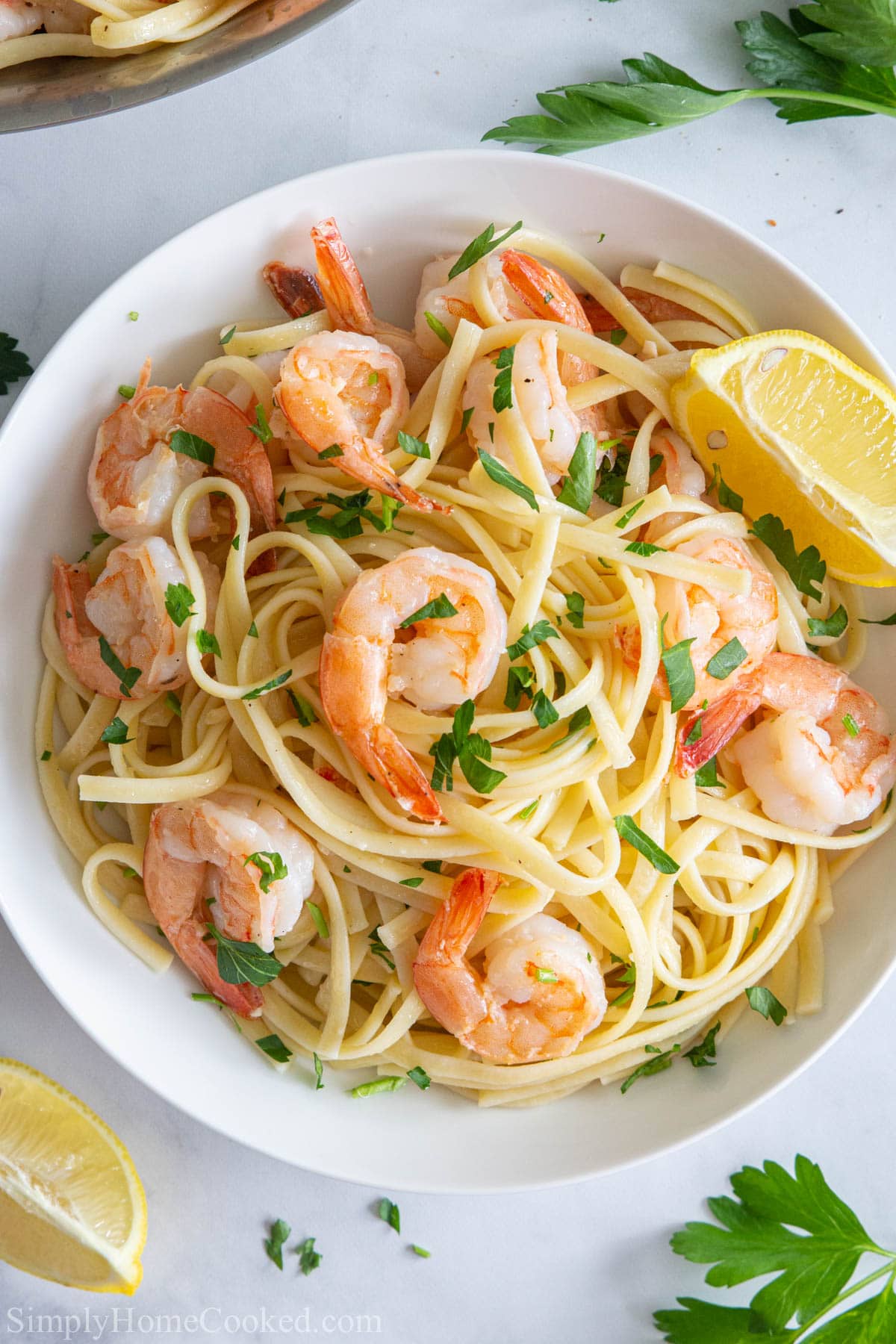 a close up of shrimp linguine in a white plate with lemons and parsley on top