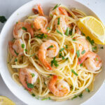 a close up of shrimp linguine in a white plate with lemons and parsley on top