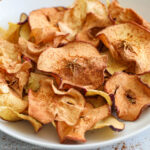 square image of air fryer apple chips on a white plate with cinnamon on top
