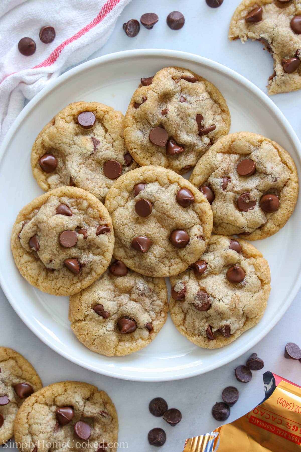 Vertical image of a plate of Chewy Chocolate Chip Cookies with cookies and chocolate chips scattered nearby.