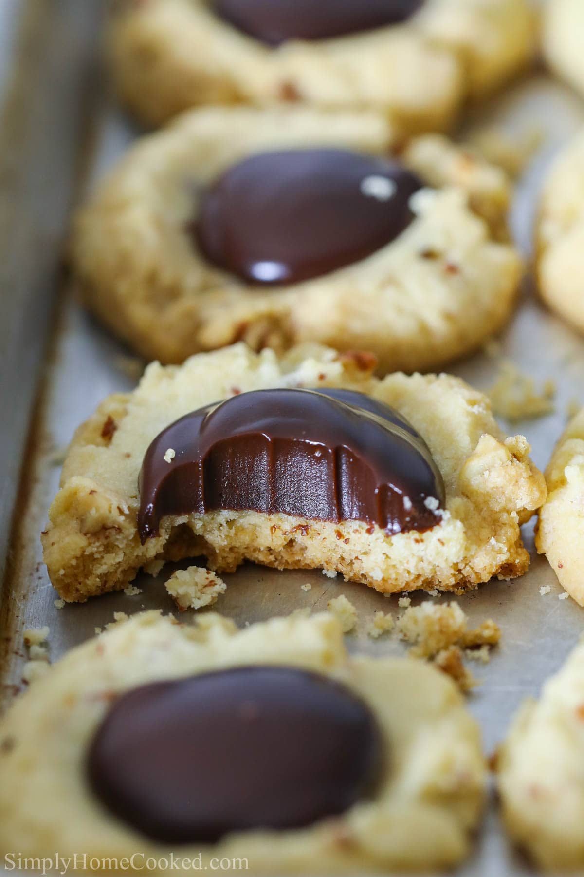 Vertical image of Chocolate Thumbprint Cookies lined up on a pan, and a close up on one missing a bite