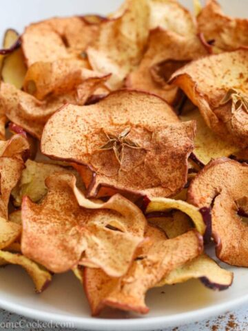 square image of air fryer apple chips on a white plate with cinnamon on top