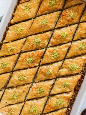 Vertical image of Baklava in a baking pan with honey on the side.