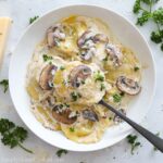 square overhead image of saucy mushroom ravioli in a white plate with herbs on top