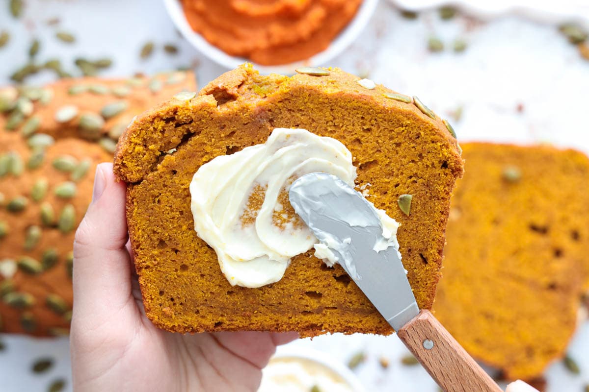 Horizontal image of a Pumpkin Bread slice being spread with butter