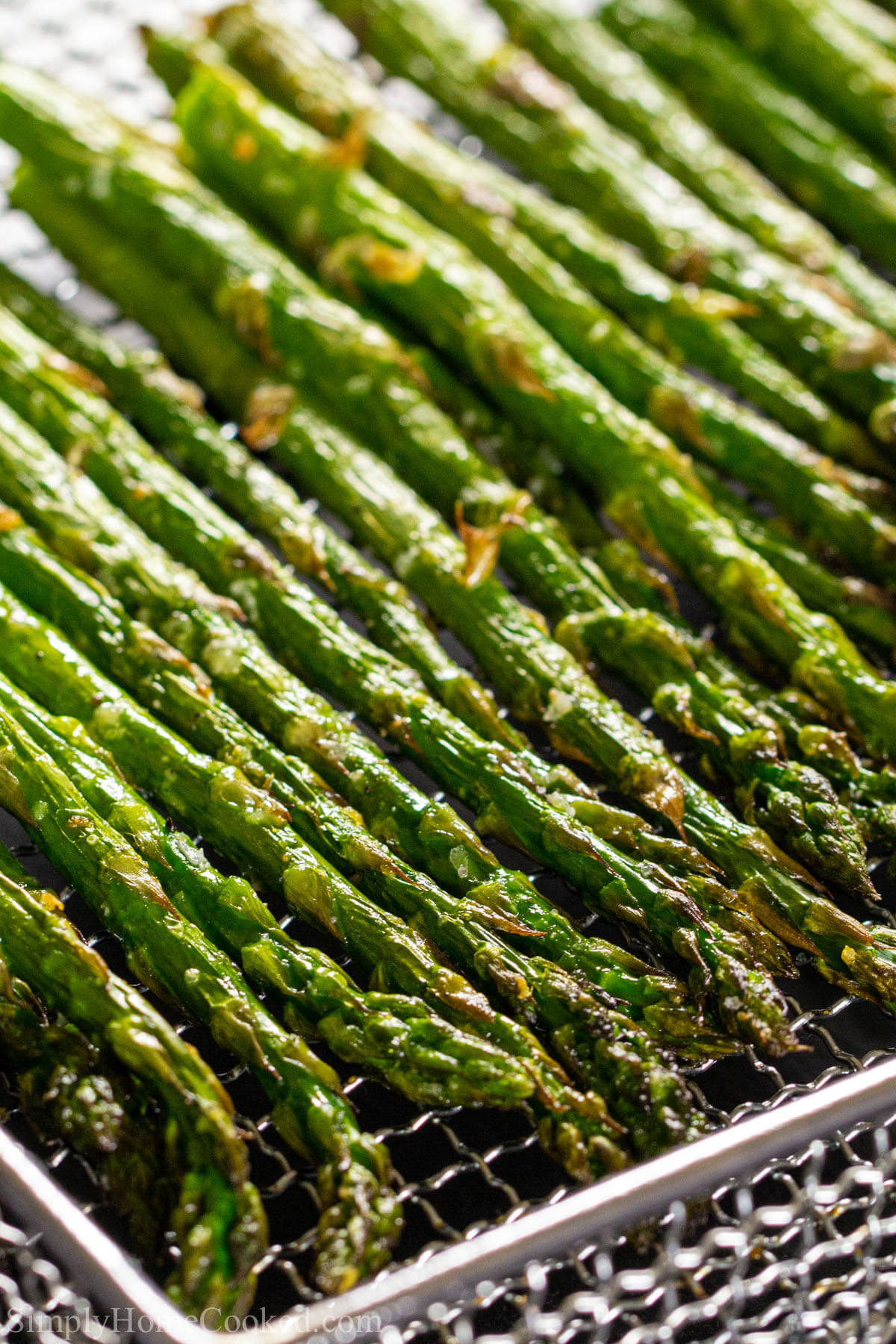 Vertical image of Air Fryer Asparagus lined up in a pan
