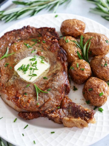 Vertical image of Juicy Air Fryer Steak with butter and potatoes on a white plate