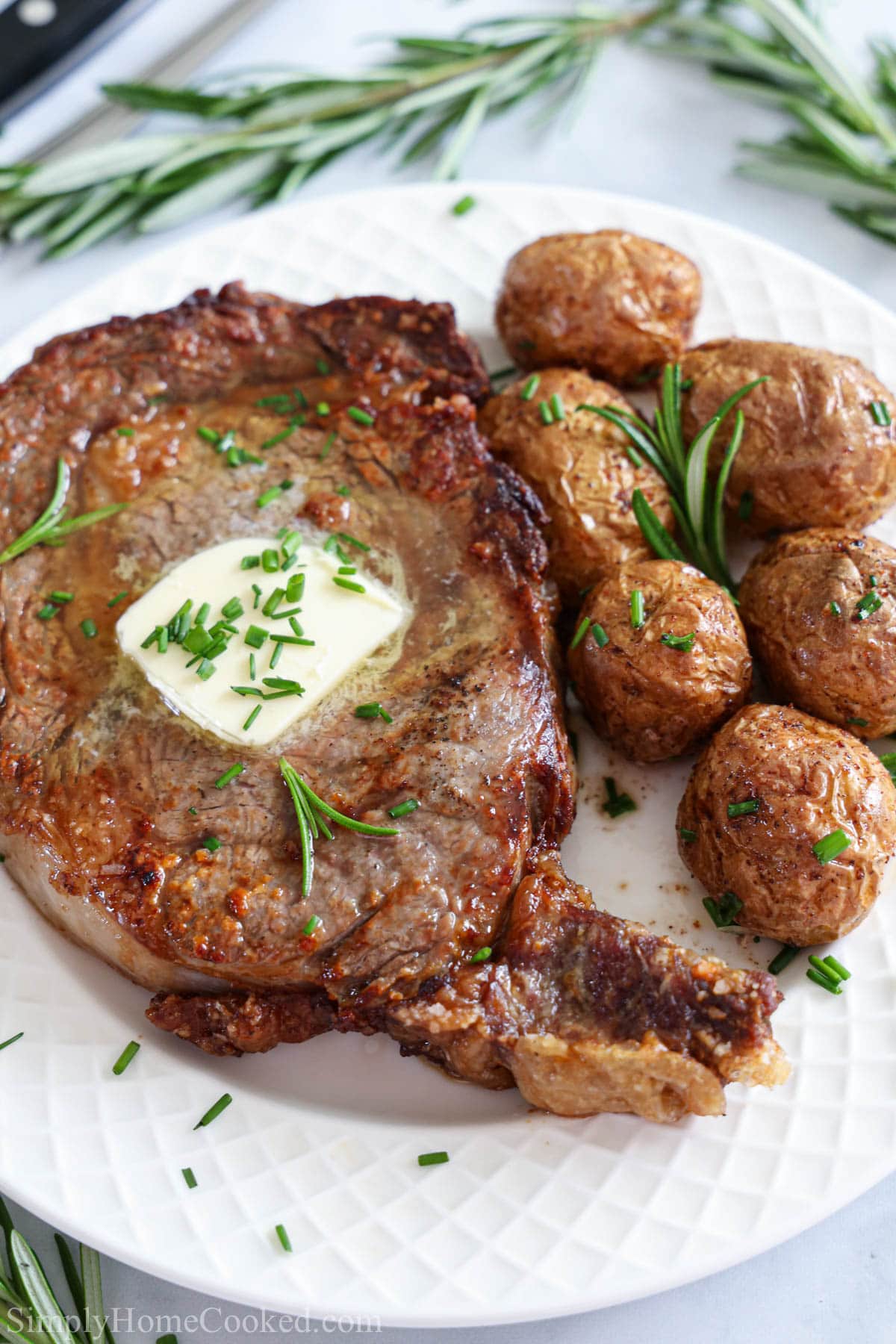 Vertical image of Juicy Air Fryer Steak with butter and potatoes on a white plate