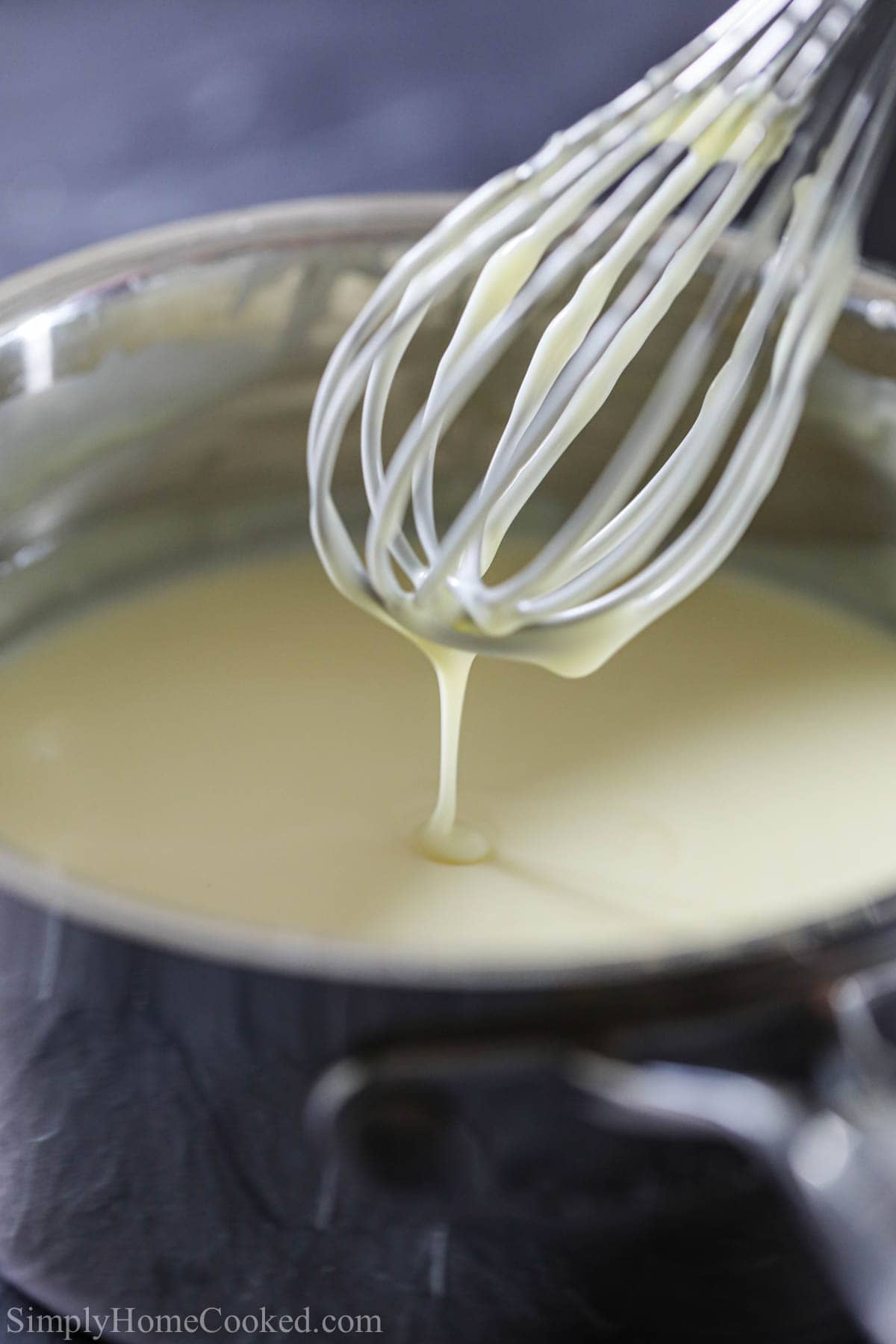 Vertical image of Bread Pudding Sauce drizzling off a whisk into a pot.