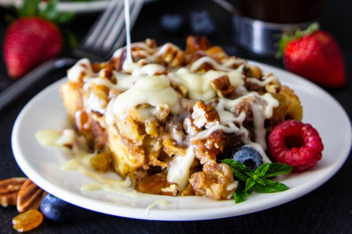 Horizontal image of Bread Pudding Sauce being drizzled onto bread pudding with berries on a plate.