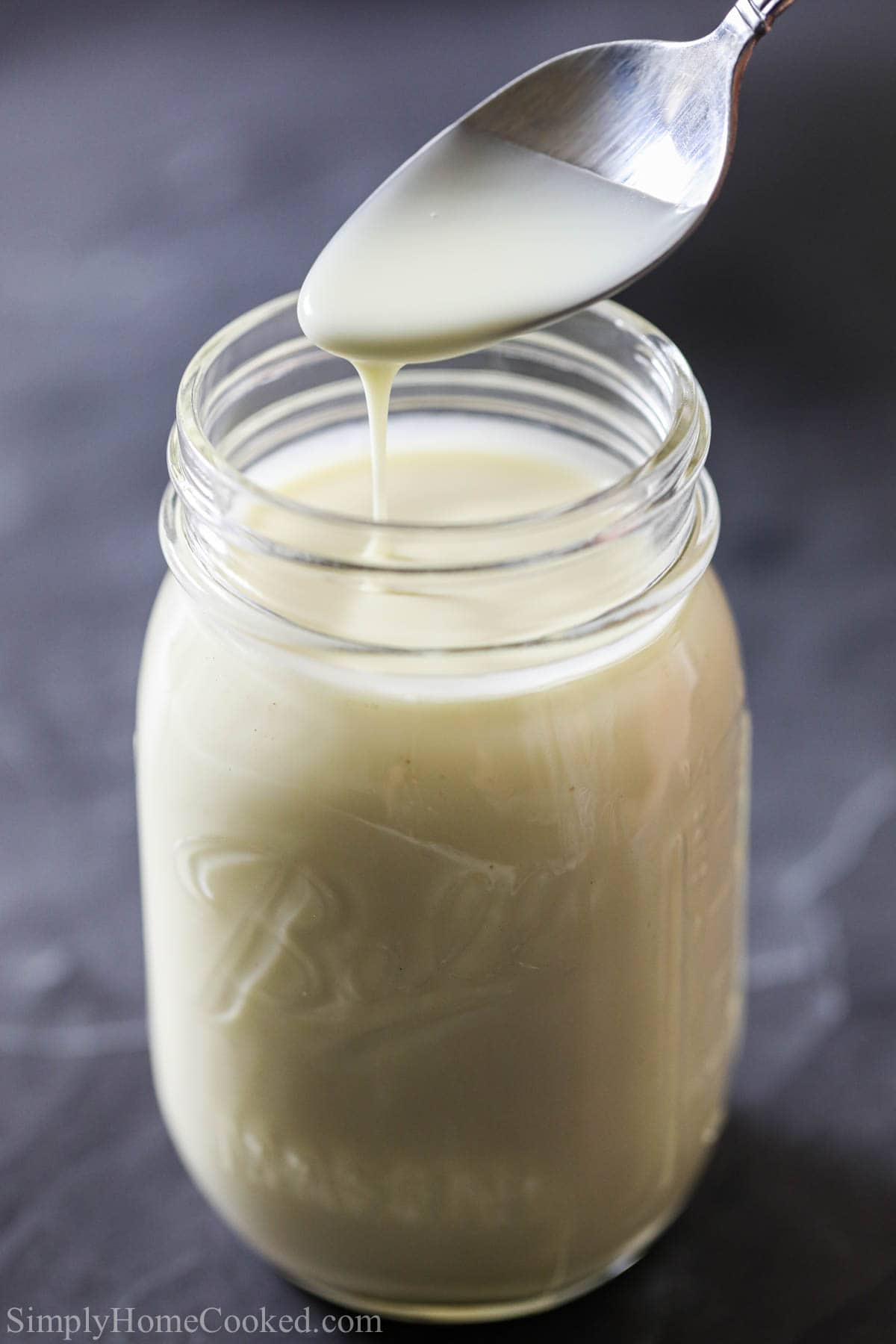 Vertical image of Bread Pudding Sauce being drizzled off a spoon into a mason jar.