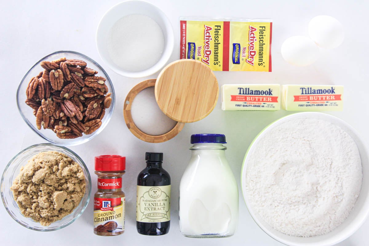 Ingredients for Best Homemade Cinnamon Rolls, including flour, sugar, yeast, butter, salt, vanilla, milk, cinnamon, brown sugar, and pecans.