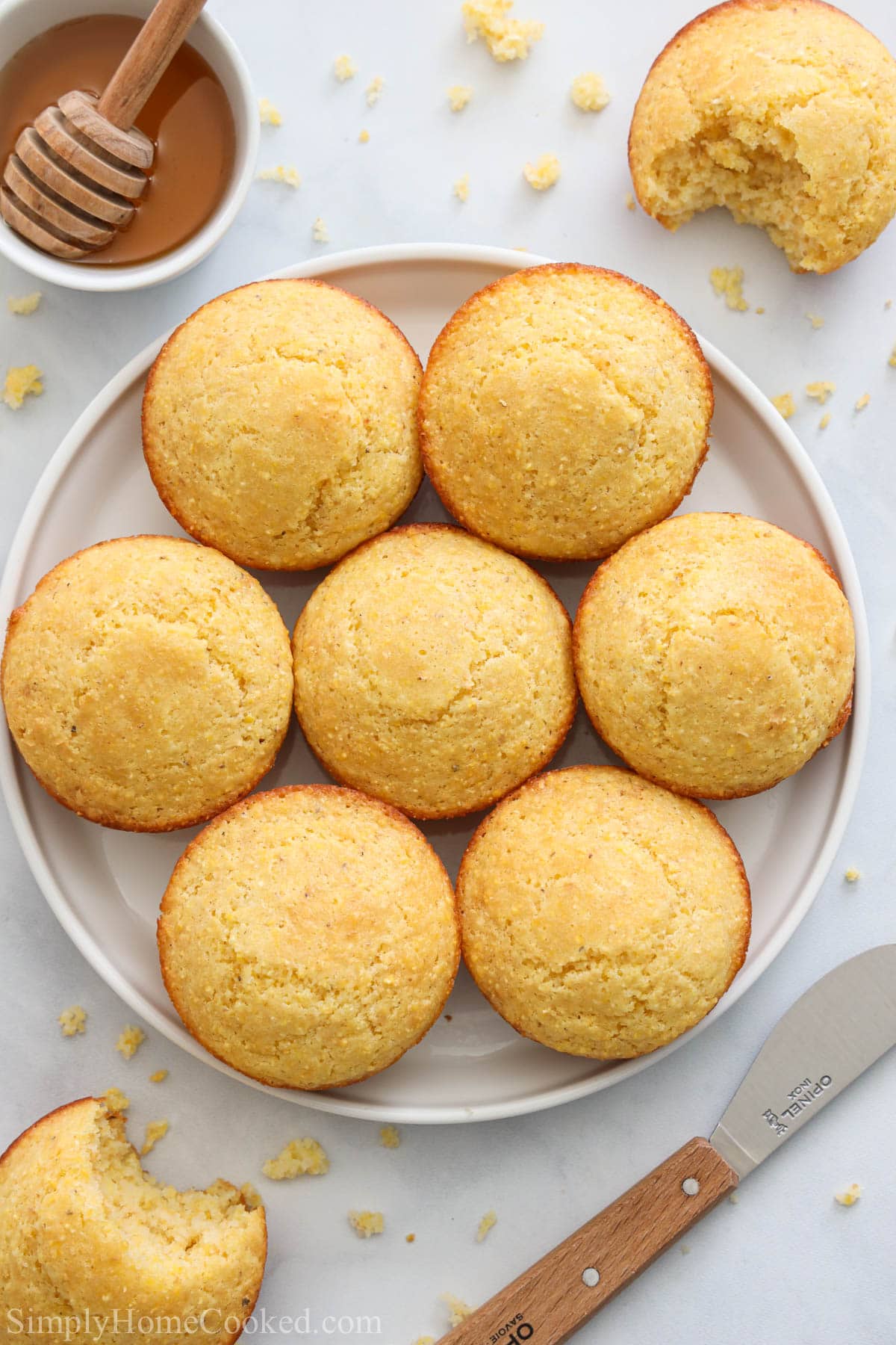 Vertical image of Cornbread Muffins on a white plate with honey and a knife nearby