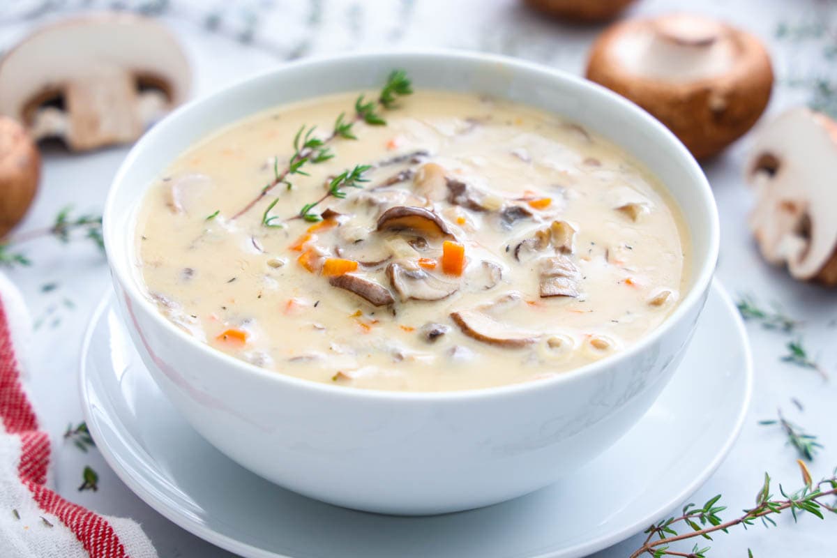 Horizontal image of Cream of Mushroom Soup in a white bowl with mushrooms in the background