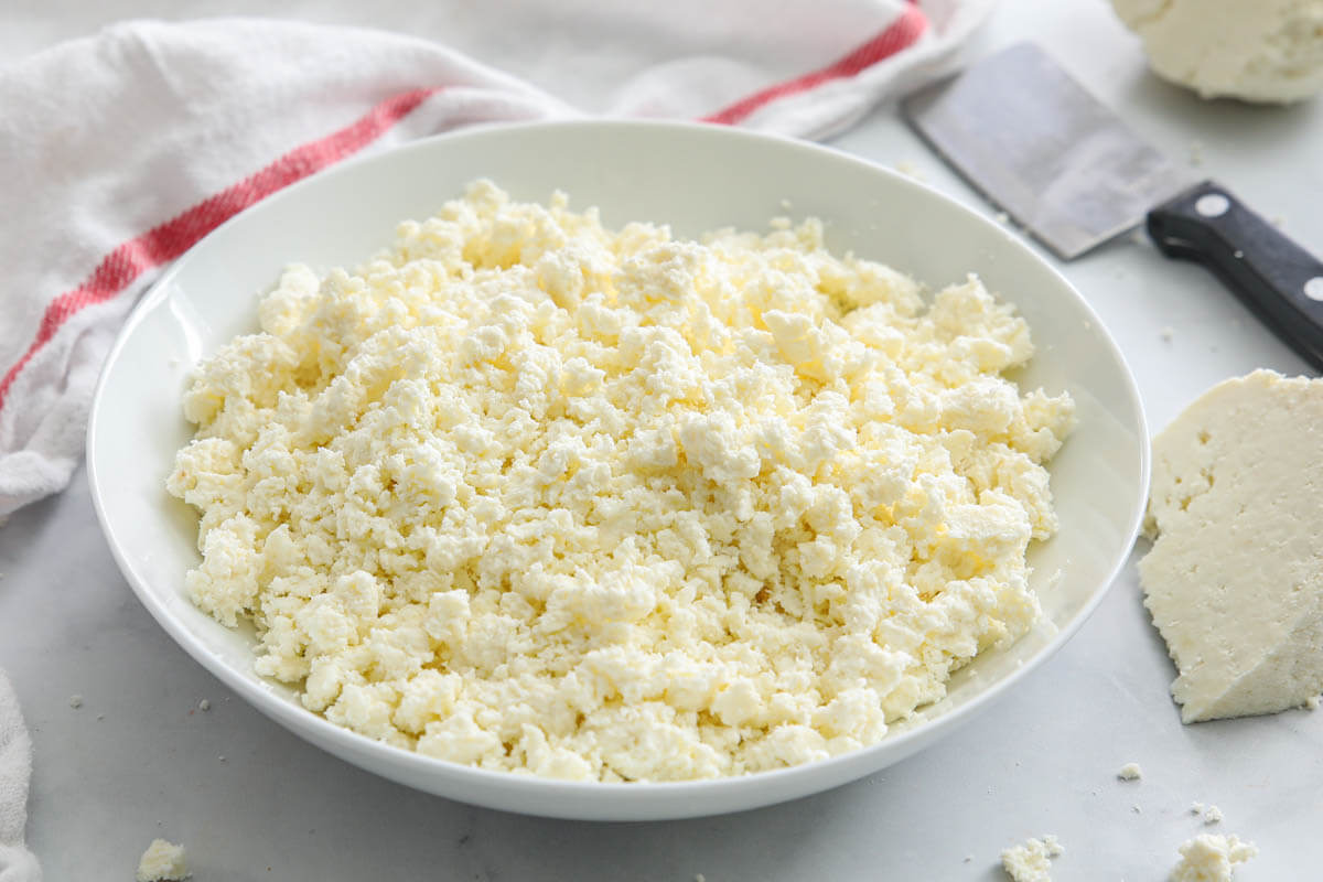 Horizontal image of Farmer's Cheese crumbles with a slice and knife nearby