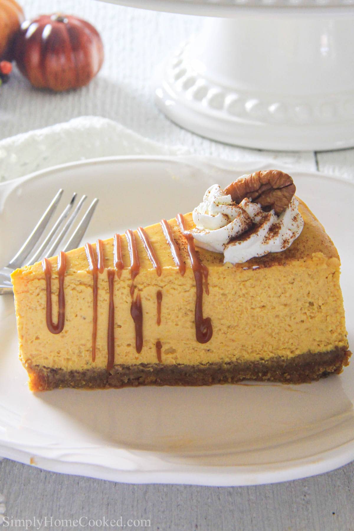 A slice of Pumpkin Cheesecake topped with pecans, caramel sauce, and whipped cream