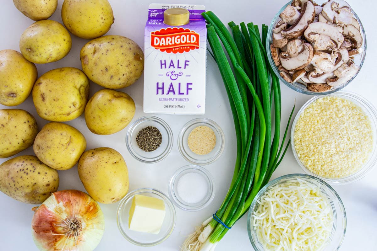 Ingredients for Scalloped Potatoes, including Yukon potatoes, yellow and green onion, cremini mushrooms, parmesan cheese, mozzarella, half & half, butter, salt, pepper, and garlic powder.