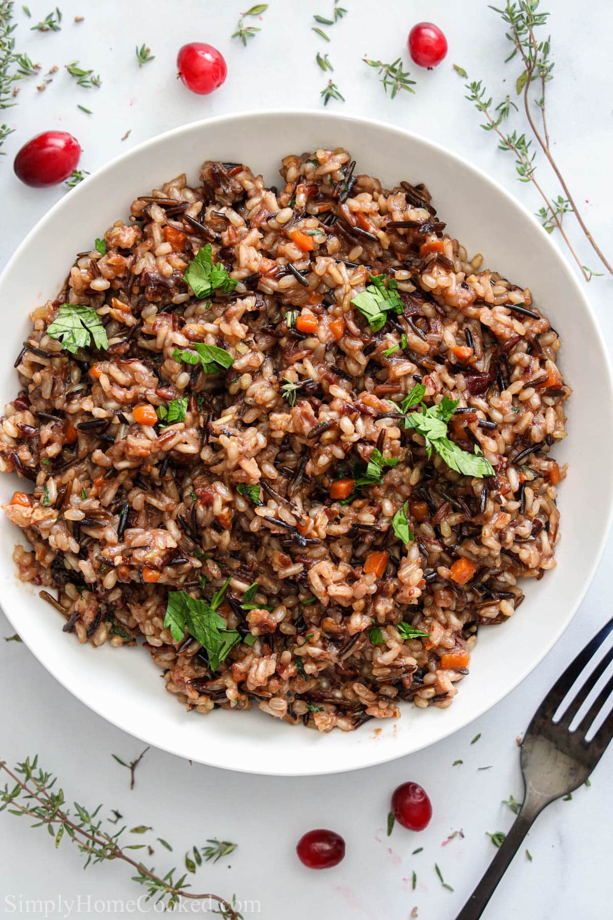 A bowl of Wild Rice with a fork, springs of thyme, and cranberries nearby