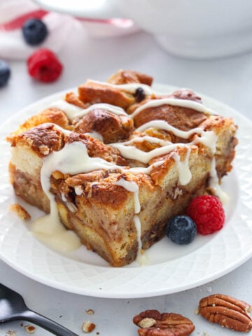 a slice of Bread Pudding covered in vanilla rum sauce on a plate with berries.