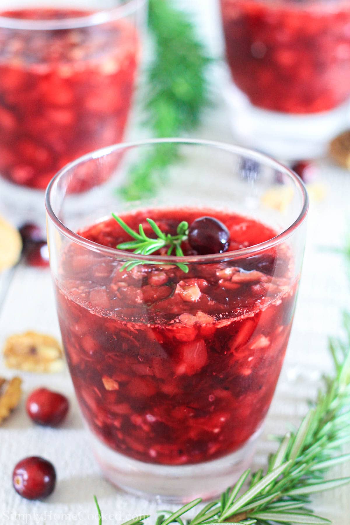 Vertical image of Cranberry Jello Salad lifted in a cup and topped with a fresh cranberry and sprig of rosemary