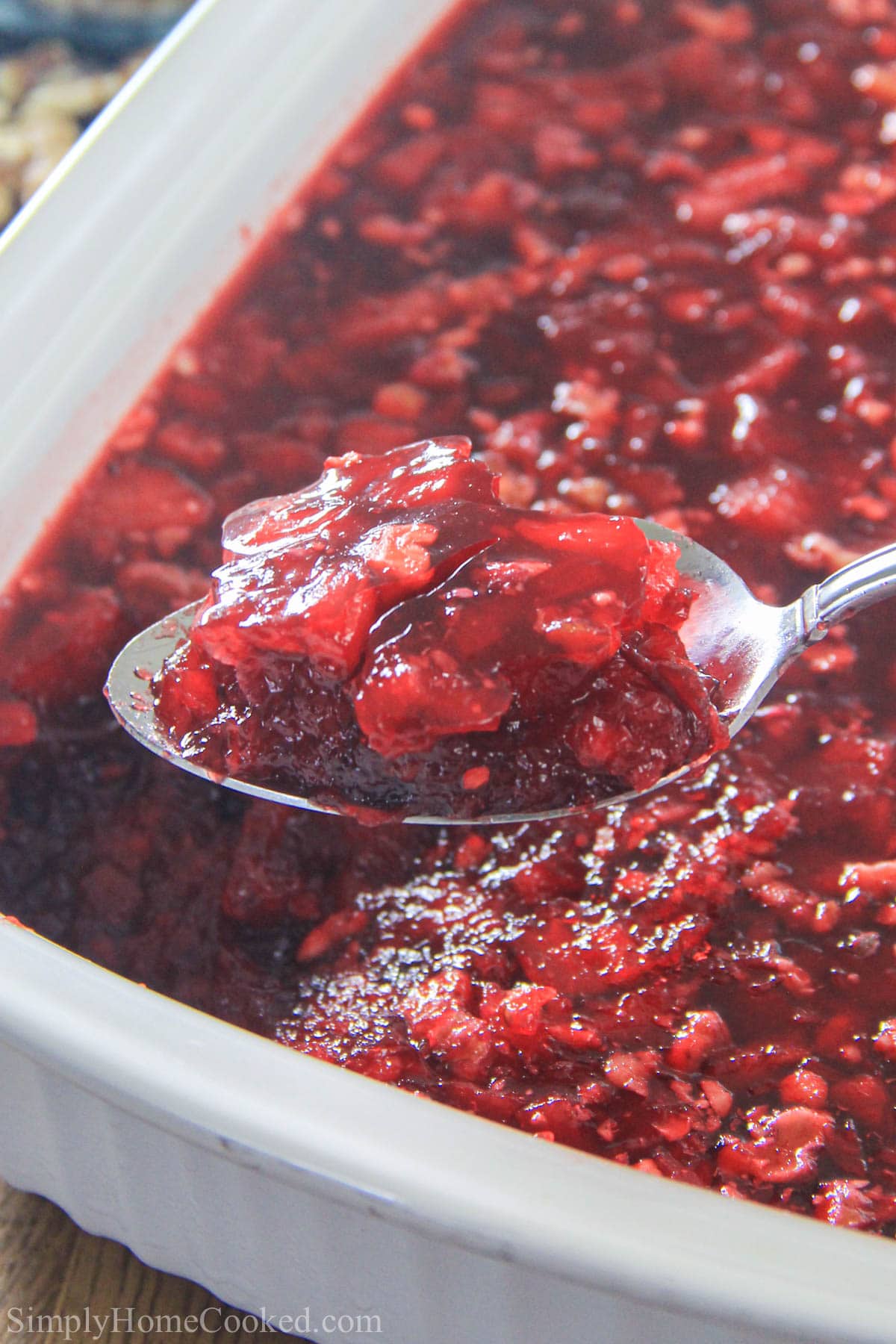 Vertical image of a spoonful of Cranberry Jello Salad lifted from a pan