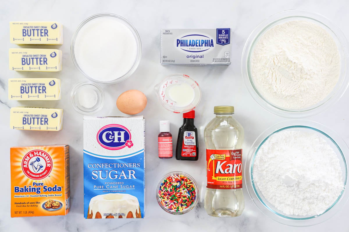 Ingredients for Lofthouse Frosted Sugar Cookies, including butter, cream cheese, baking soda, baking powder, salt, sugar, flour, eggs, corn syrup, vanilla, oil, powdered sugar, sprinkles, milk, and food coloring.