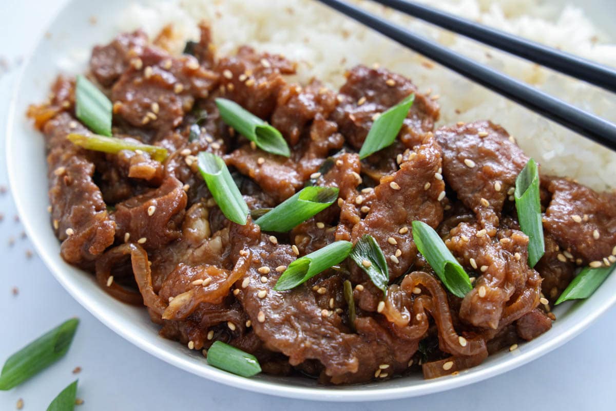 Horizontal image of Mongolian Beef  with green onions and rice on a white plate with black chopsticks