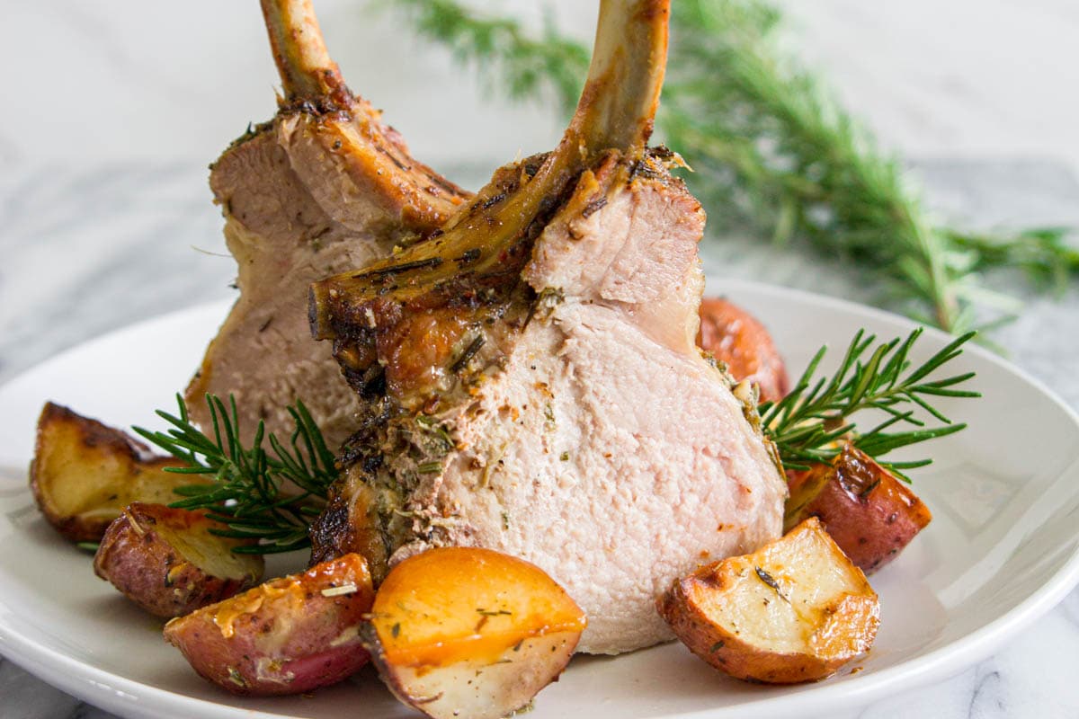 Horizontal image of two pieces of Pork Crown Roast on a plate with rosemary and potatoes.