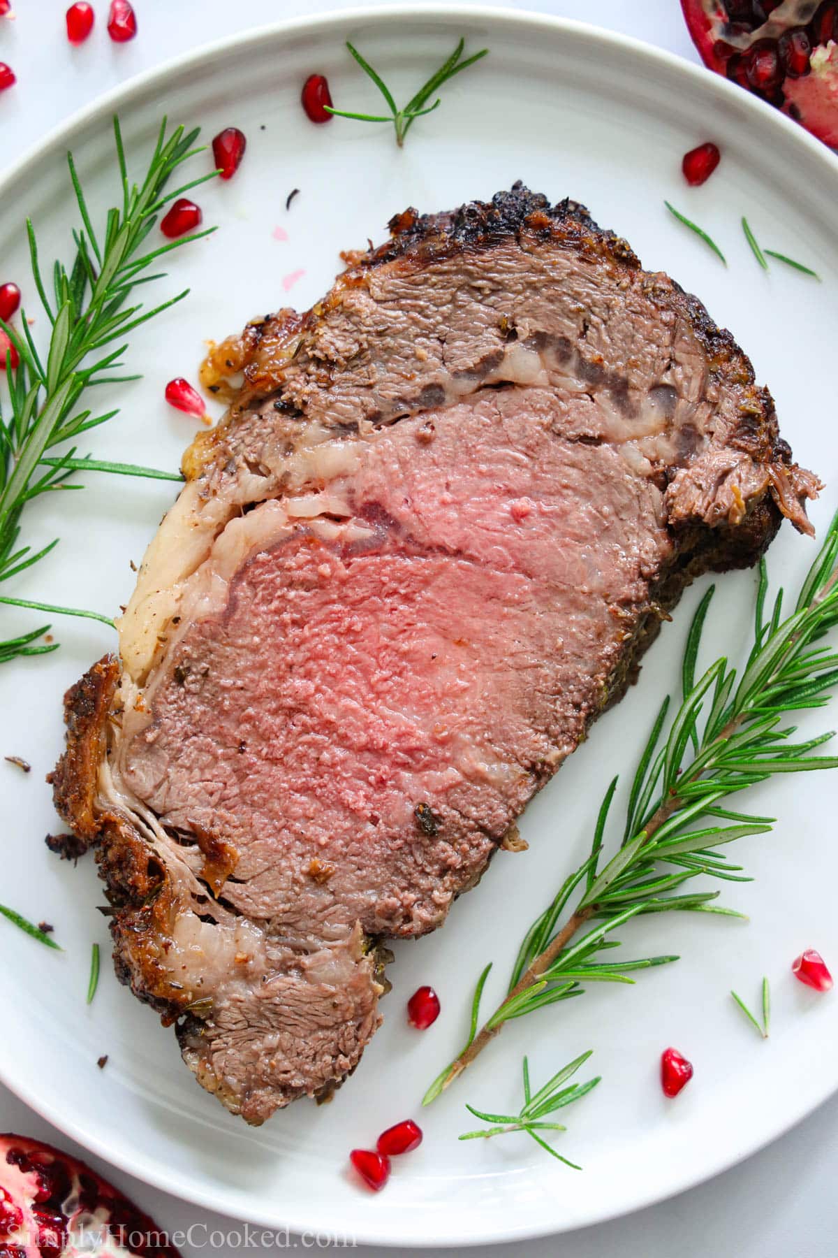 a slice of prime rib on a white plate with rosemary and pomegranate seeds