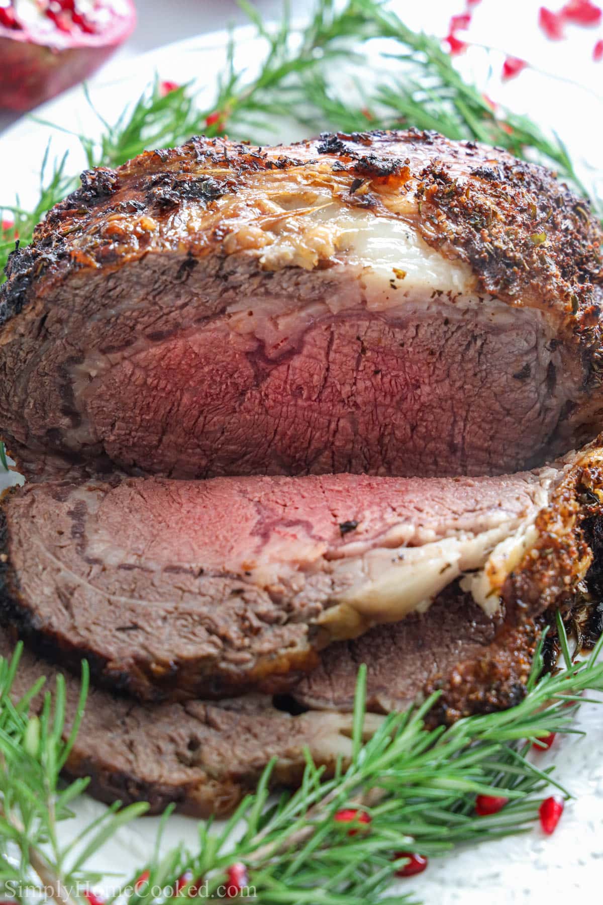 Prime Rib sliced on a plate with herbs and pomegranate seeds