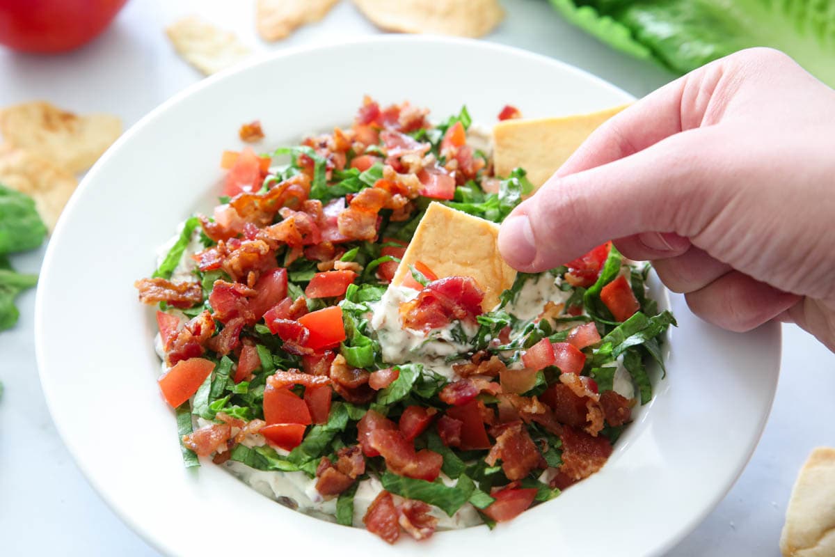 Horizontal image of a bowl of Easy BLT Dip with a pita cracker being dipped in