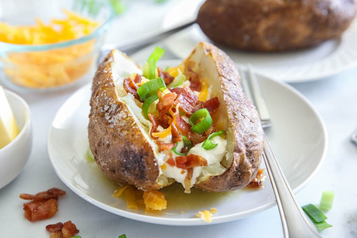 Horizontal image of Air Fryer Baked Potato with toppings on a white plate, and a fork nearby